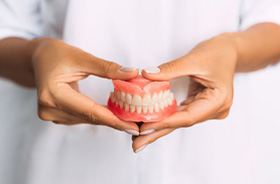 Person in white coat holding full set of dentures