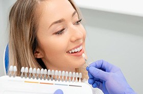 Gloved hand holding shade guide close to patient’s teeth