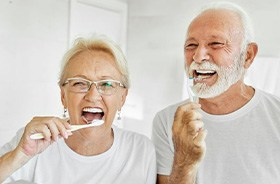 Older couple brushing their teeth in front of bathroom mirror