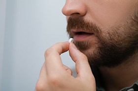 Man preparing to swallow a small white pill